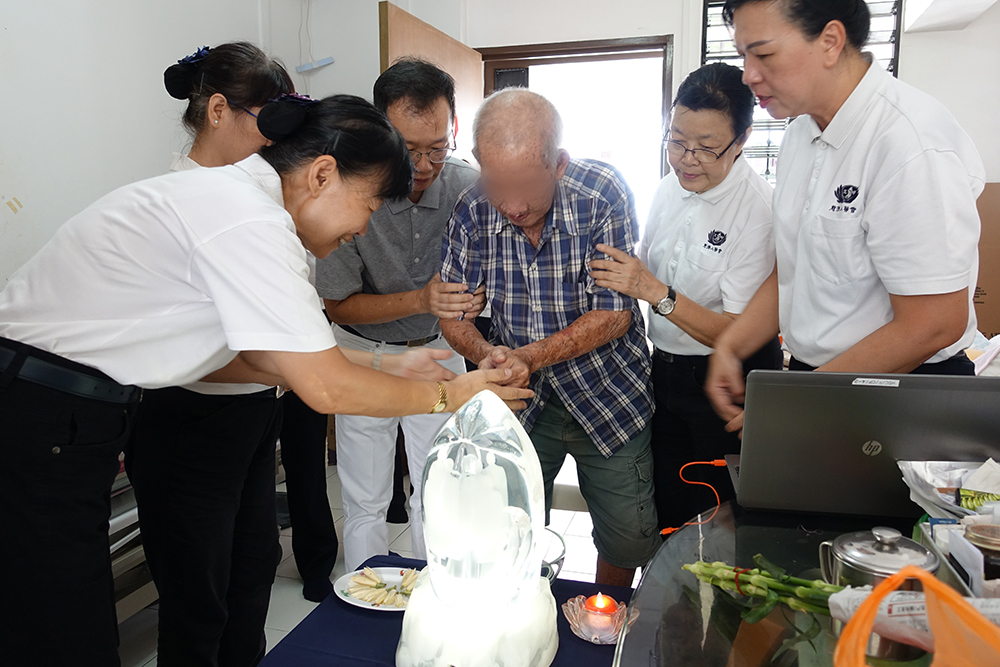 Madam Tan’s husband performing the Buddha Bathing ritual with the guidance of Tzu Chi’s medical staff and volunteers.